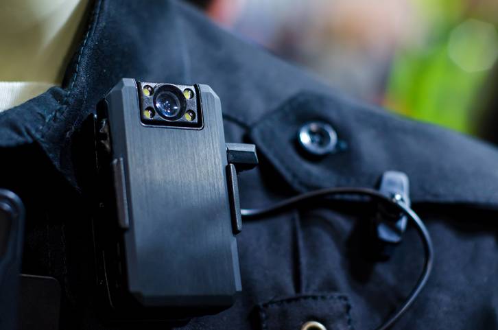 A police officer's uniform is equipped with a black body cam, securely attached near the shoulder area, highlighting modern law enforcement technology used during arrests.