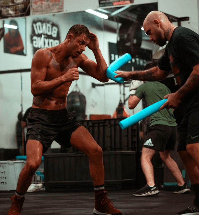 Danilo Dash Creati working on technique with a coach using foam sticks in a boxing gym.