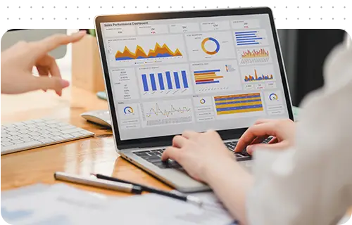 A hand points to a laptop screen displaying various charts and graphs, suggesting collaboration or analysis.