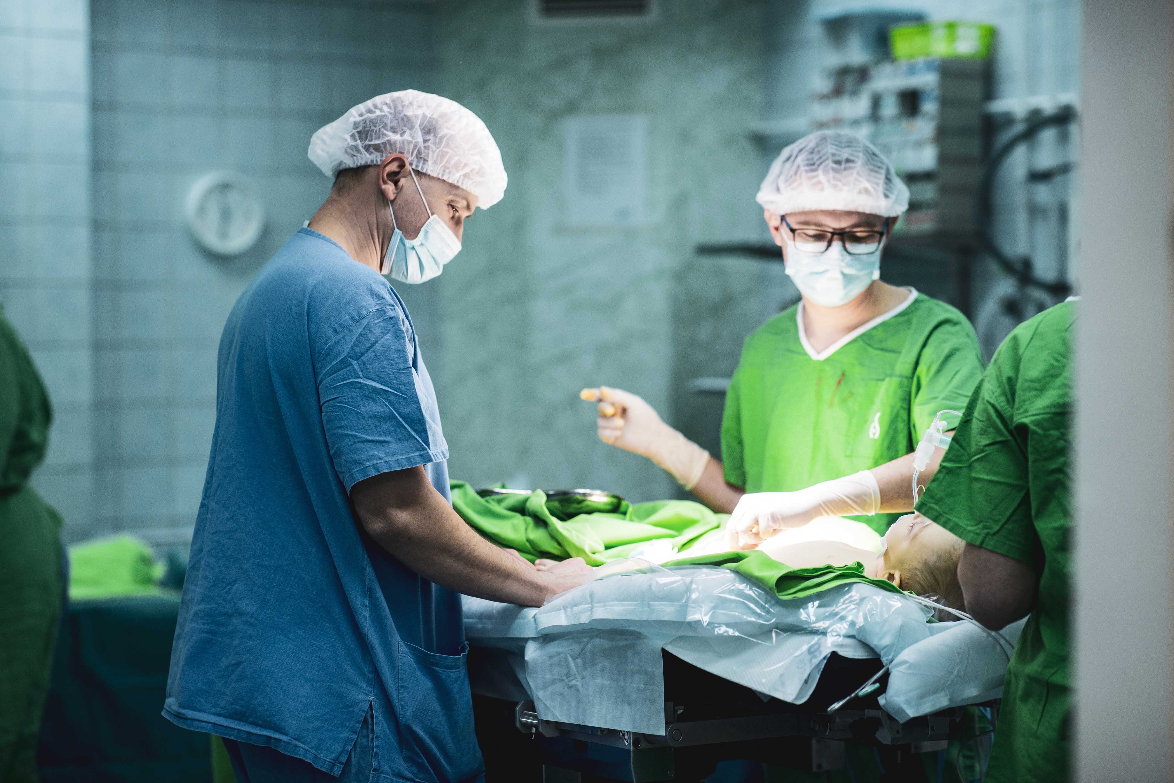 Két sebész operál egy műtőasztalon fekvő pácienst, műtősruhában és maszkban.