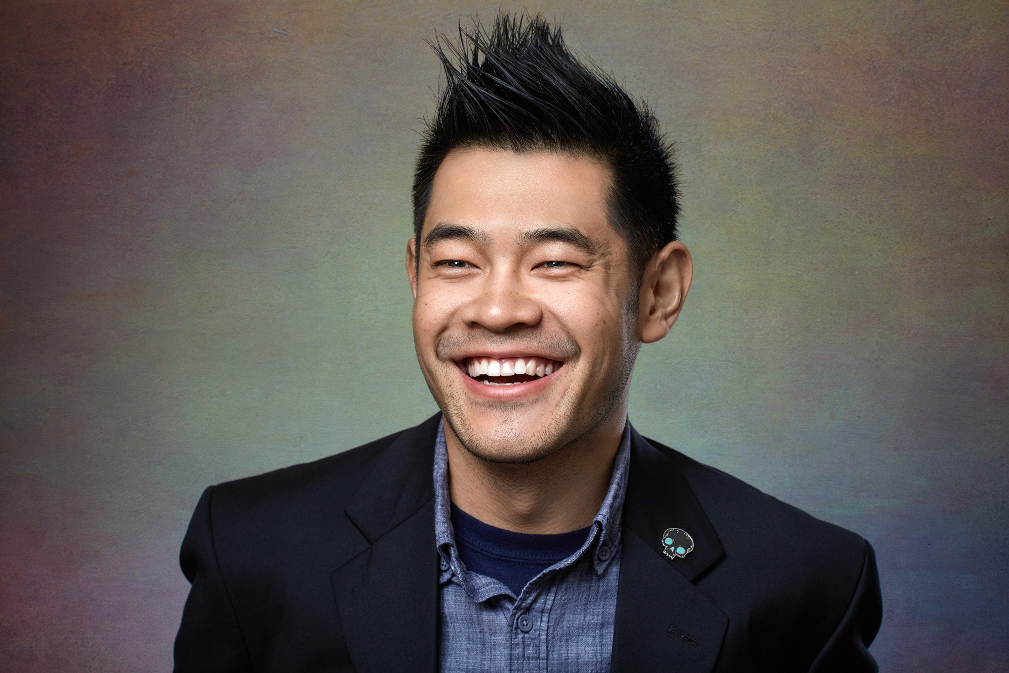 Candid laughing headshot of a man in a grey tee, capturing a genuine unscripted moment. The signature character portrait style.