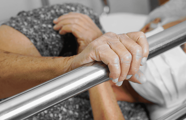 Elderly patient gripping a bed rail while lying in a hospital bed.