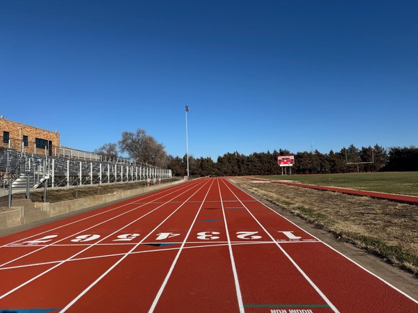 Red track straightaway with painted lane numbers and bleachers alongside