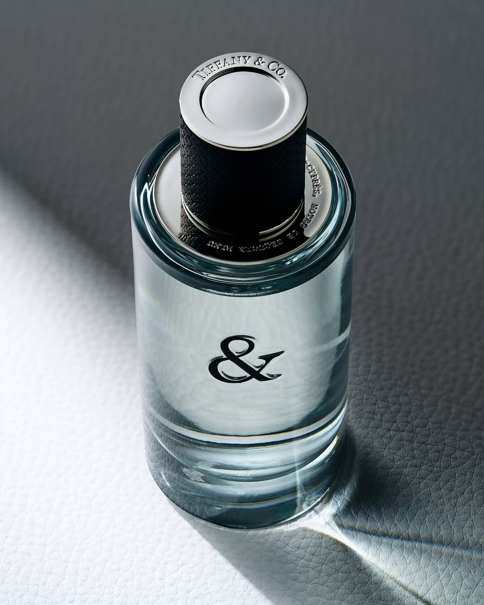 A clear glass bottle with a black cap and a white label featuring an ampersand symbol.