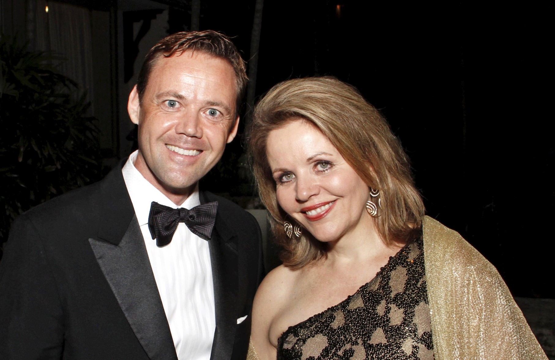 A man in a tuxedo and a woman in a formal gown smile into the camera.