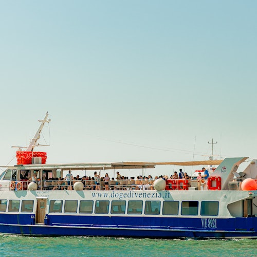 一艘蓝白相间的客运渡轮载满乘客，在晴朗天空下平静的海面上航行。