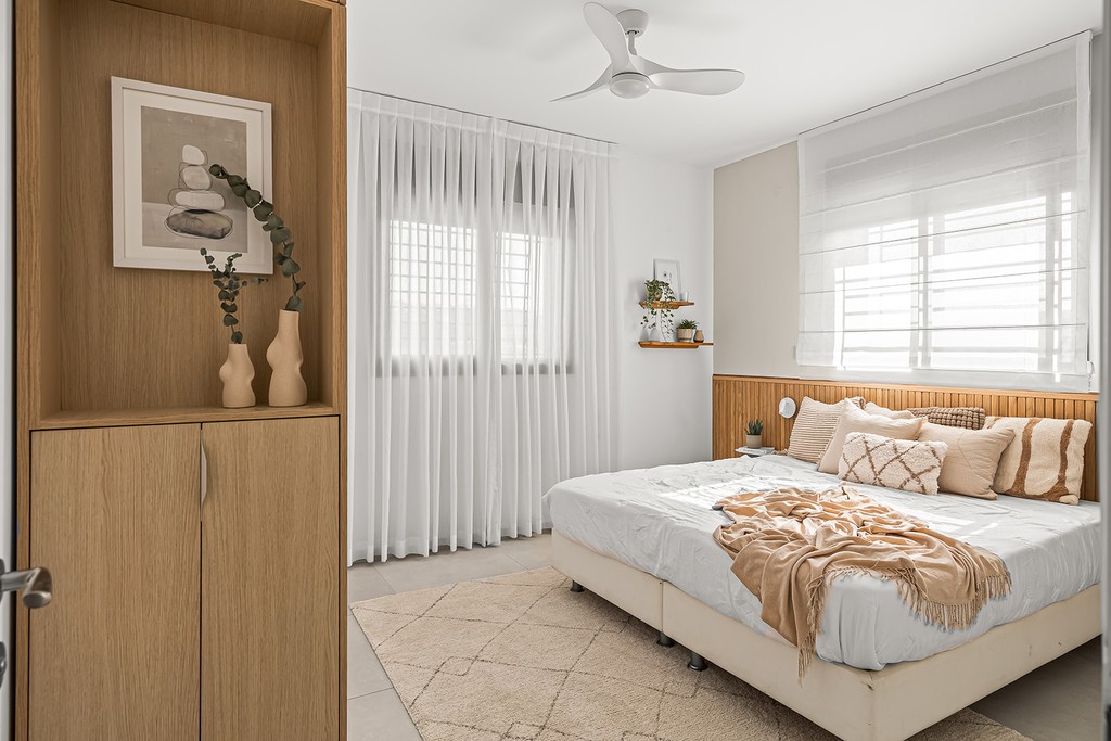 חדר שינה מודרני ומואר עם מיטה בעלת גב עץ ועיצוב בגוונים ניטרליים.