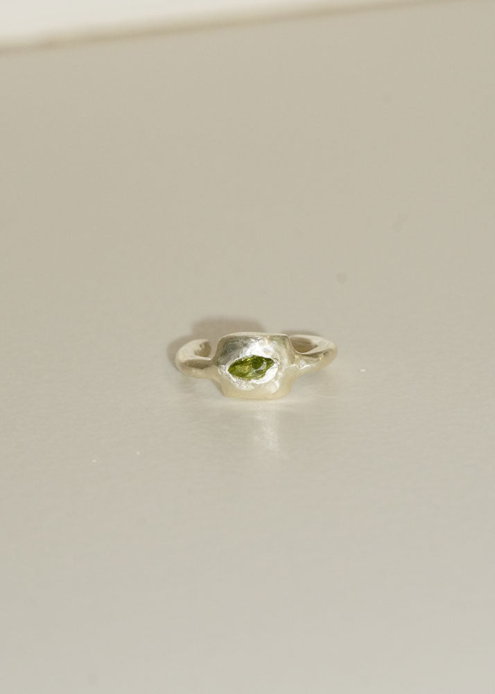 Silver ring with a green gemstone on a light beige background