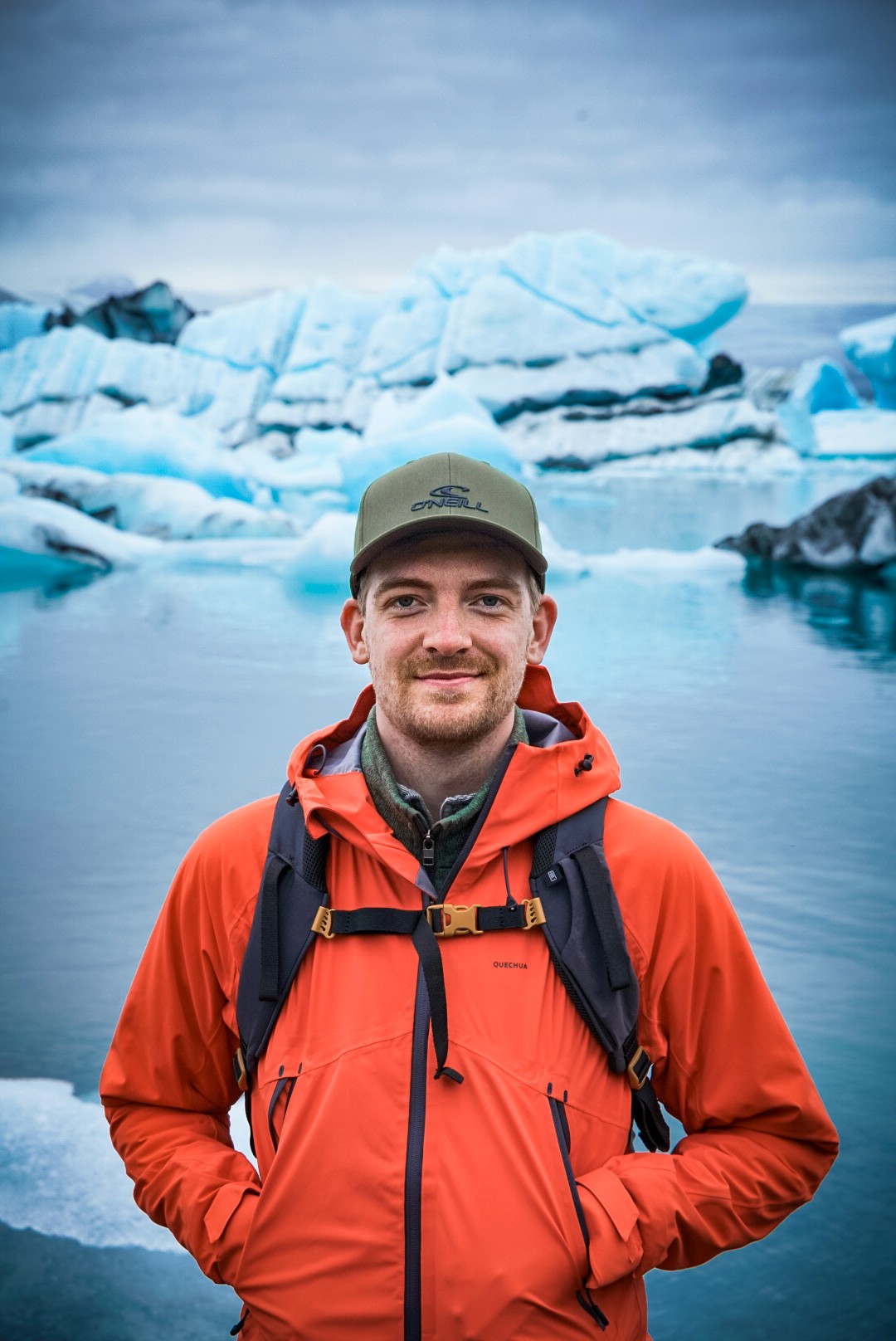 A view from an airplane window shows the aircraft's wing with a golden hue reflecting the setting sun, against a serene backdrop of fluffy clouds and a clear sky.