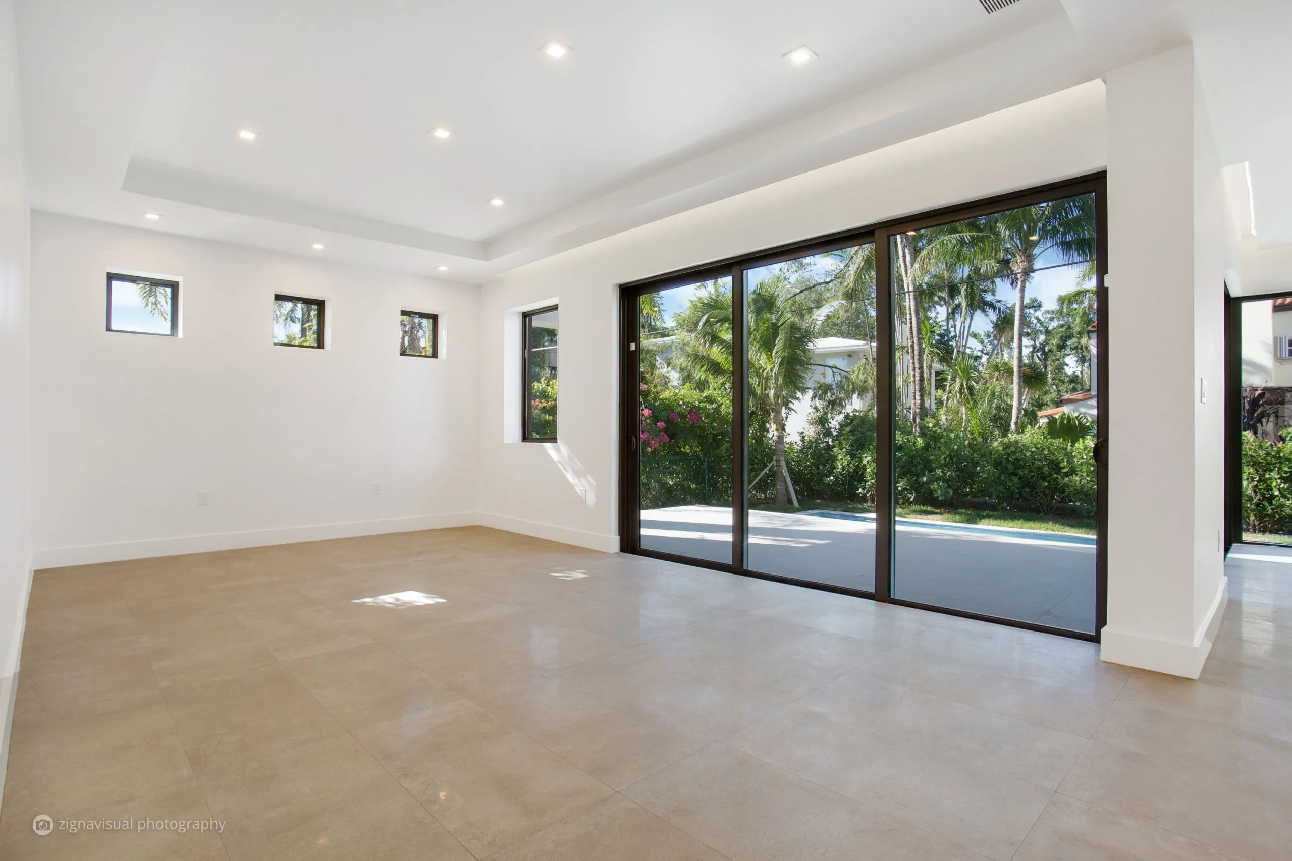 Open plan living area with floor-to-ceiling glass sliding doors in modern Miami Beach residence by Atelier International LLC