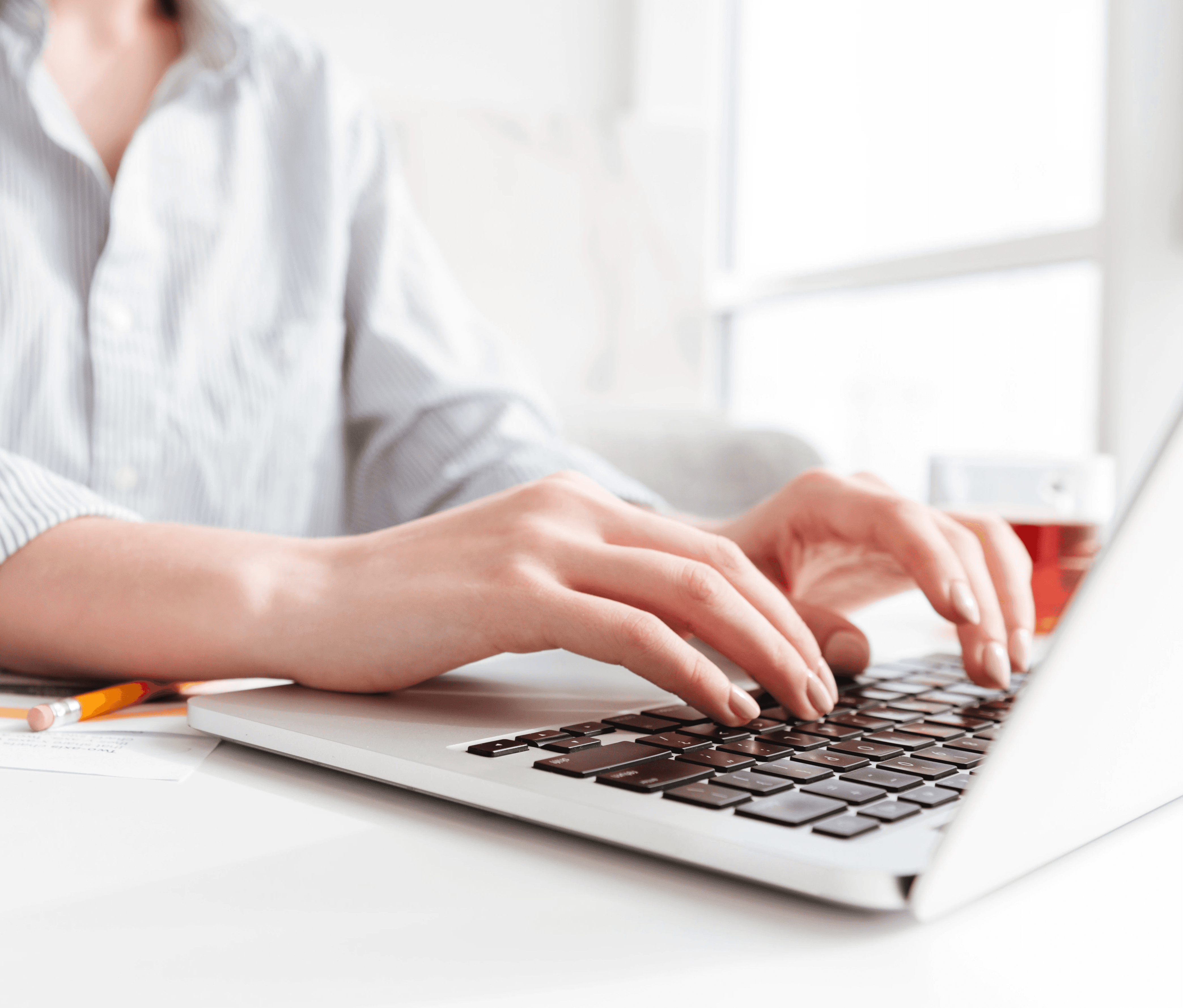 Un primer plano de las manos de una persona escribiendo en una computadora portátil en un espacio de trabajo moderno y luminoso.