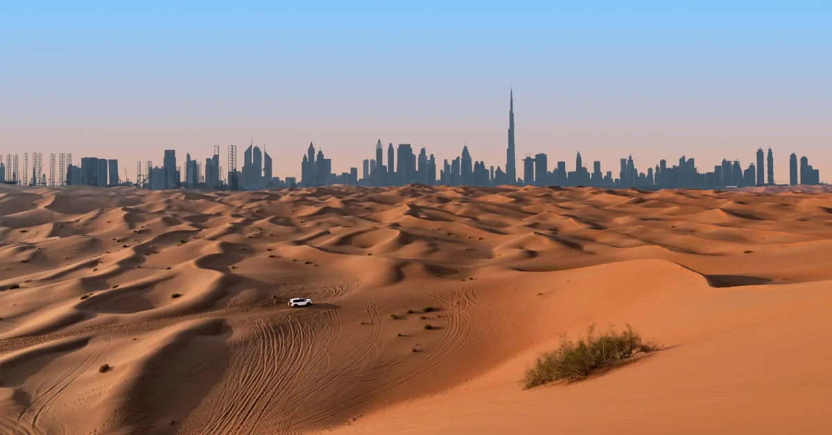 Dunas del desierto en primer plano con el skyline de Dubái y el Burj Khalifa al fondo