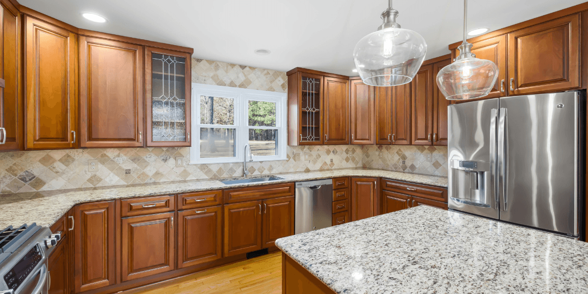 The kitchen features warm wood cabinets, granite countertops, stainless steel appliances, and elegant lighting, reflecting a modern, inviting design.