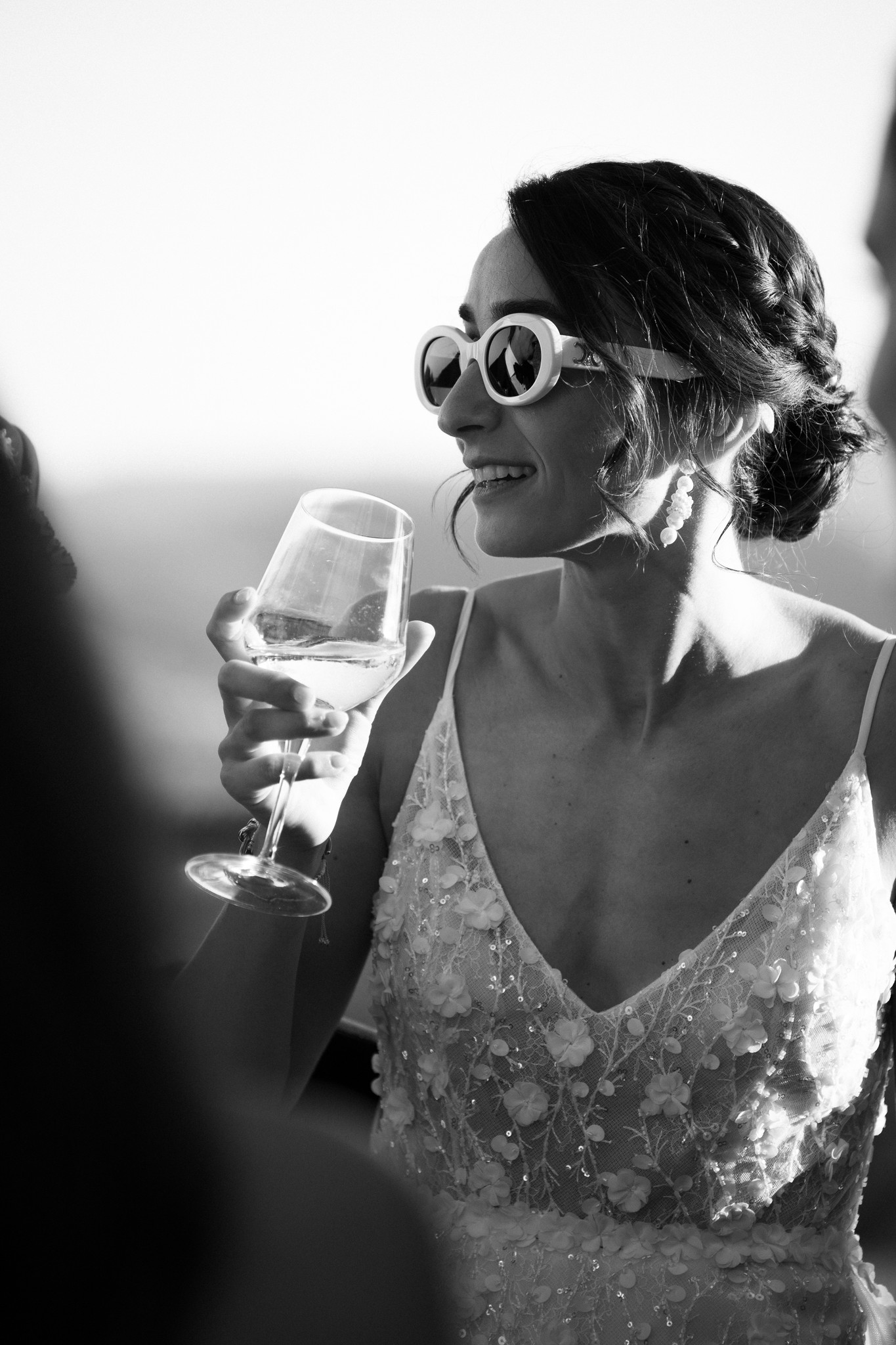 Sposa con occhiali da sole e flute di champagne sorride durante il ricevimento al Castello di Tabiano, in bianco e nero