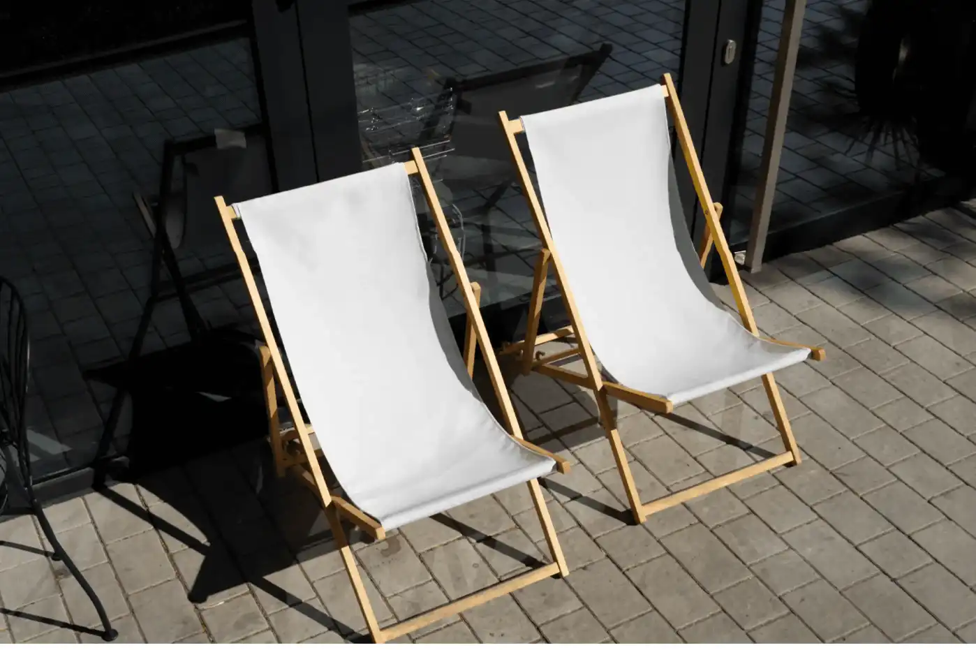 Pair of sunbed mockups with wooden frames placed on a paved outdoor area. One features a beige fabric, while the other displays a lavender design with playful graphics, creating a casual and vibrant summer setting.