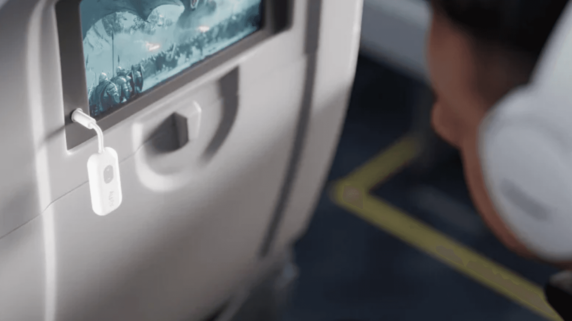 An AirFly SE connected into the screen in an airplane, with a person wearing headphones in the right hand corner.