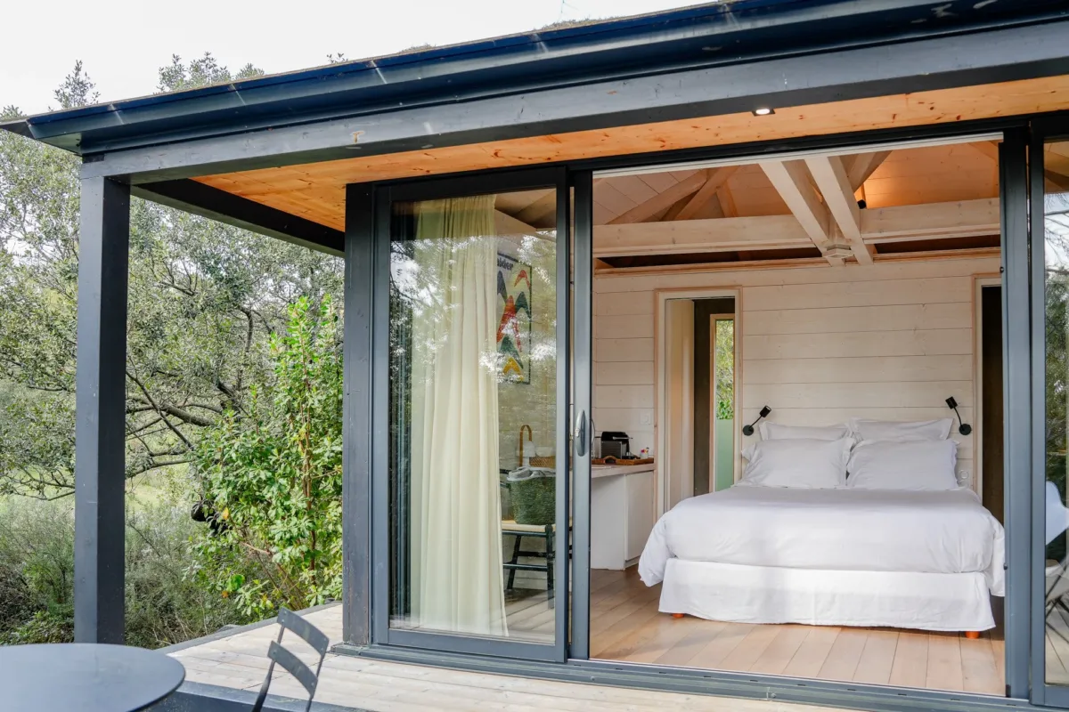 Chambre de l'écolodge Monte Verdi avec baie vitrée ouverte sur la terrasse et fauteuils papillon