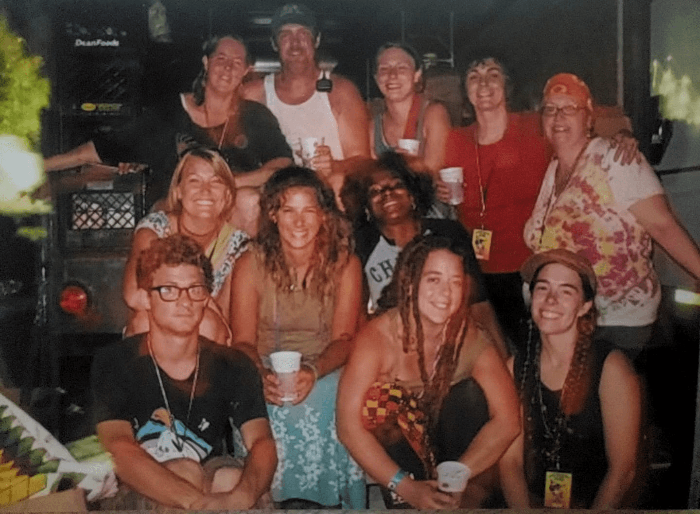 A group of twelve people working at PCS smiling and posing together in a lively indoor setting, holding drinks.