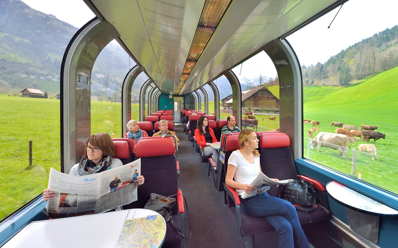 Passengers enjoying scenic view from panoramic train window in Swiss countryside.