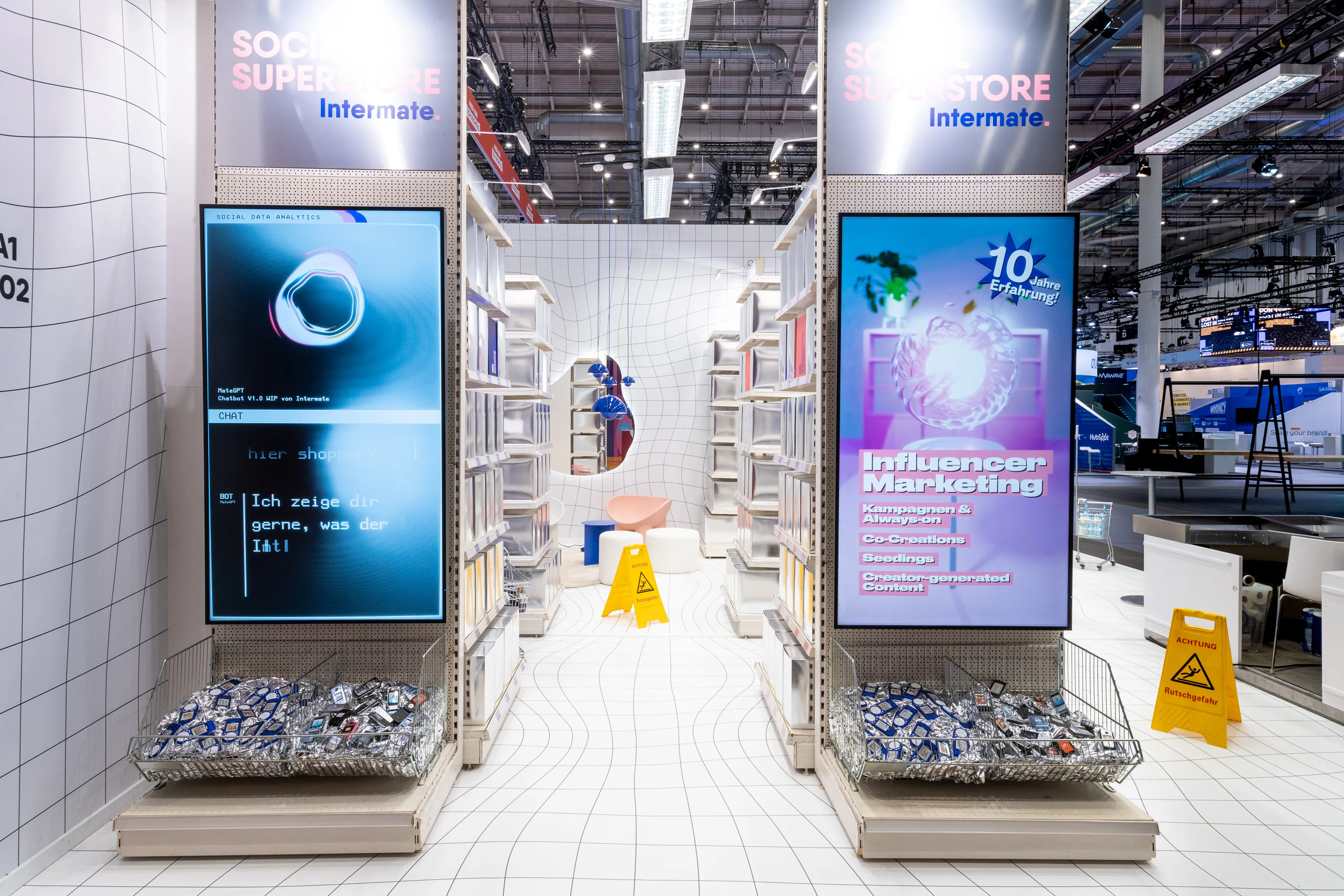 Two display gondolas with screens for chat and influencer marketing and wire baskets full of phones at the Intermate booth.