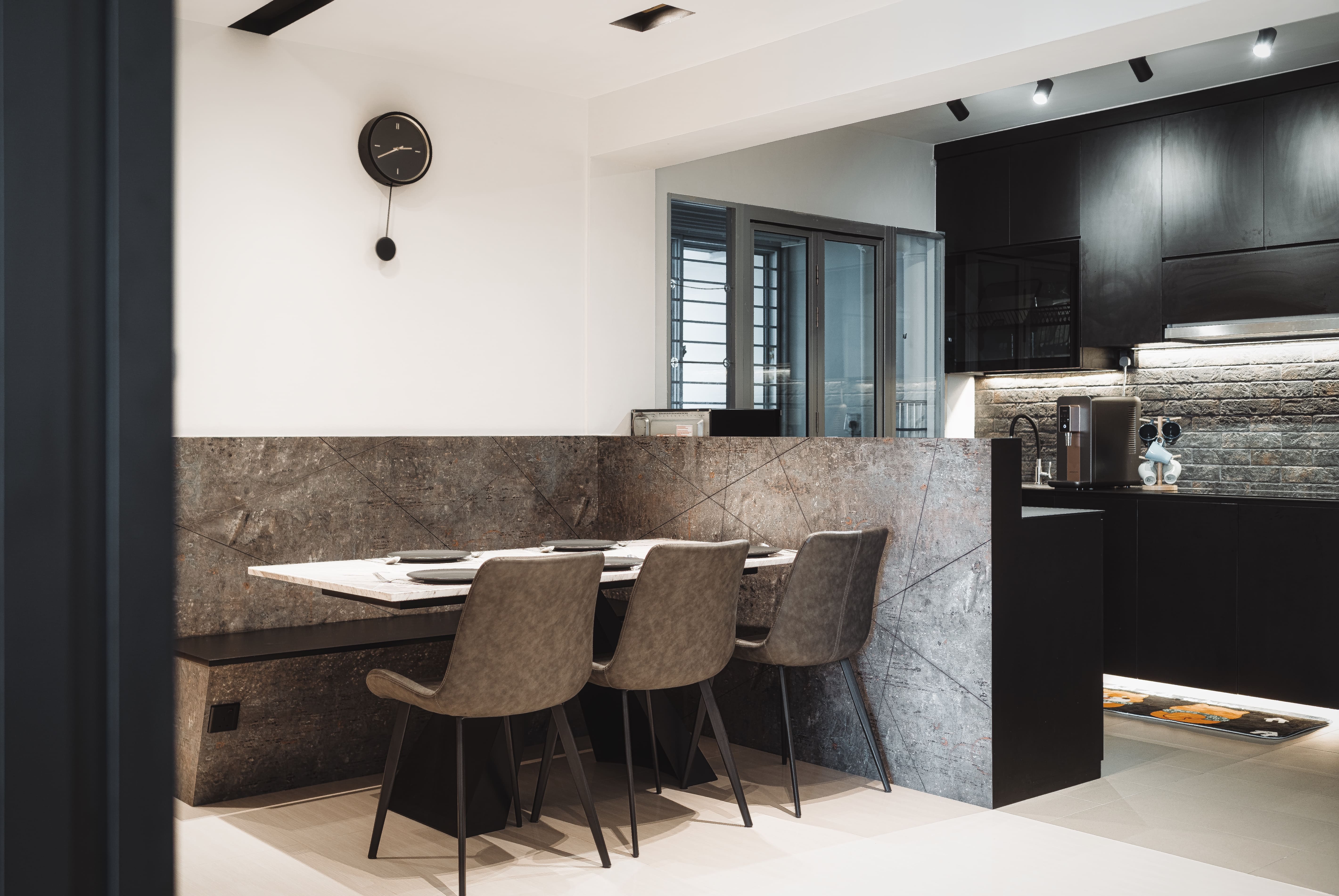 Dining nook framed in textured stone panels, paired with upholstered chairs and a minimalist wall clock.