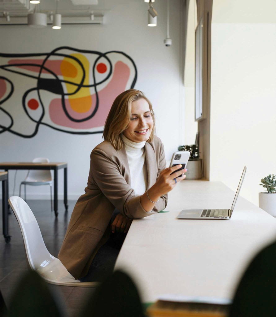 A woman smiling at her phone in a bright cafe