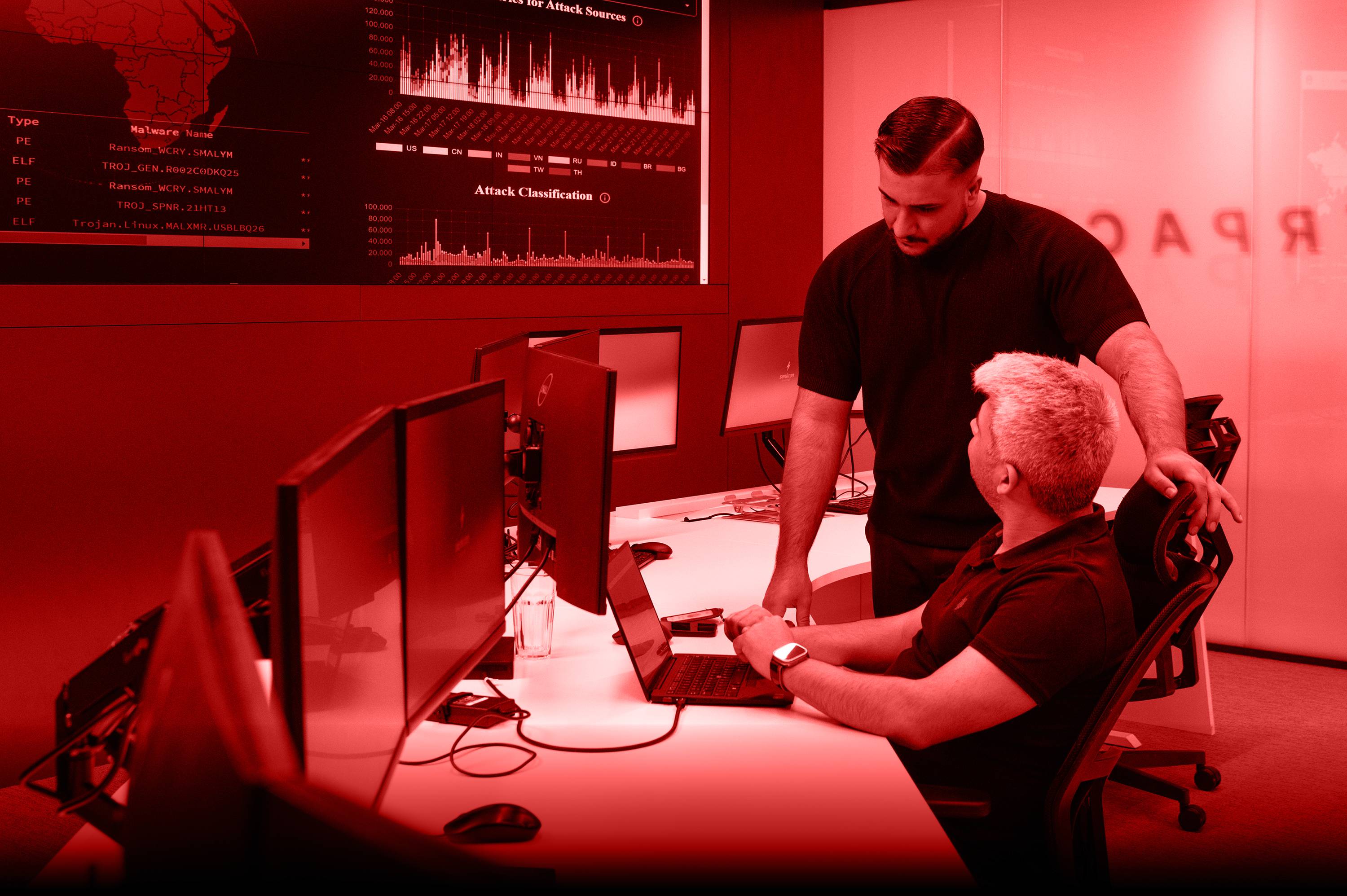 A person sits in front of multiple screens in a dimly lit control room, focused on the displays.