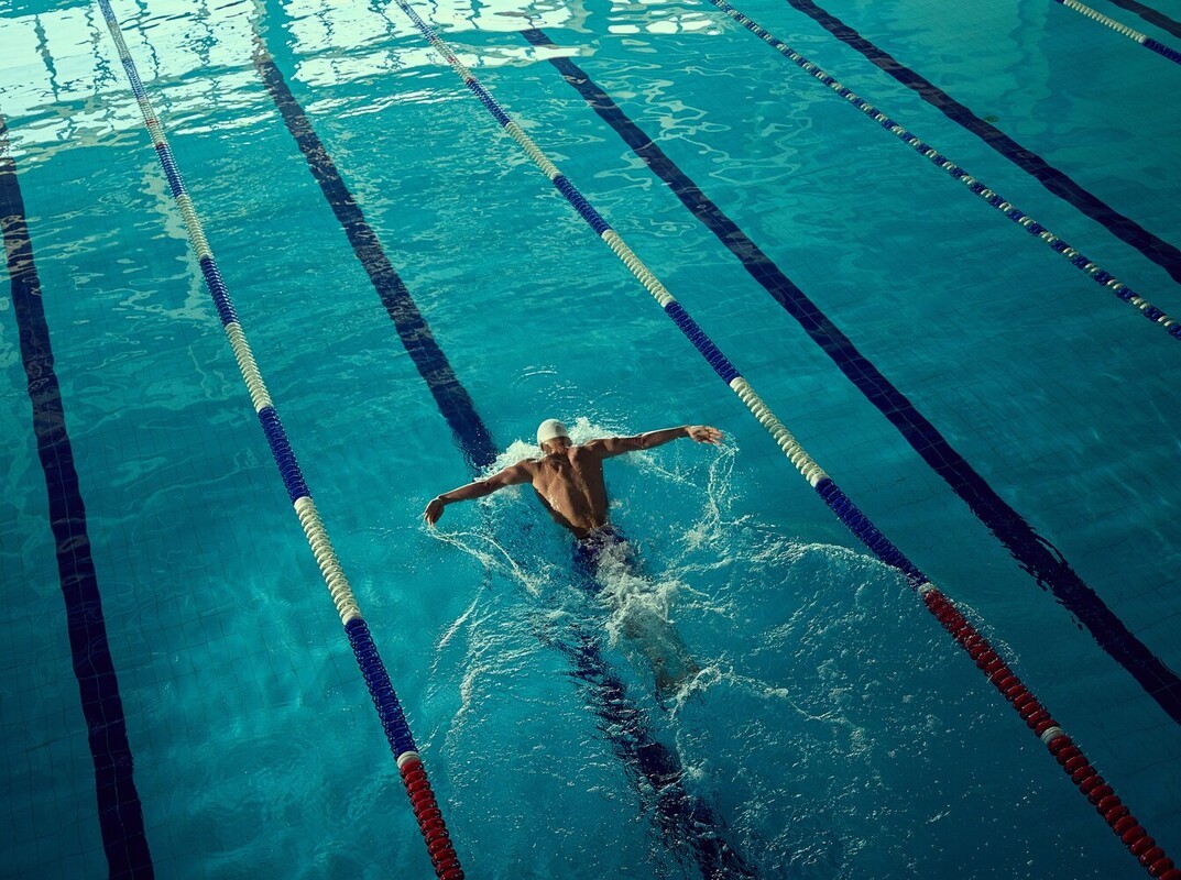 man doing the butterfly stroke during his swimming routine for weight loss in the pool at his gym