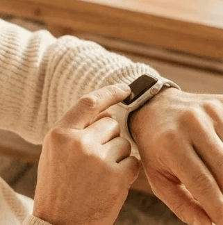 African american woman in pink cropped hoodie on the beach checking her fitness device