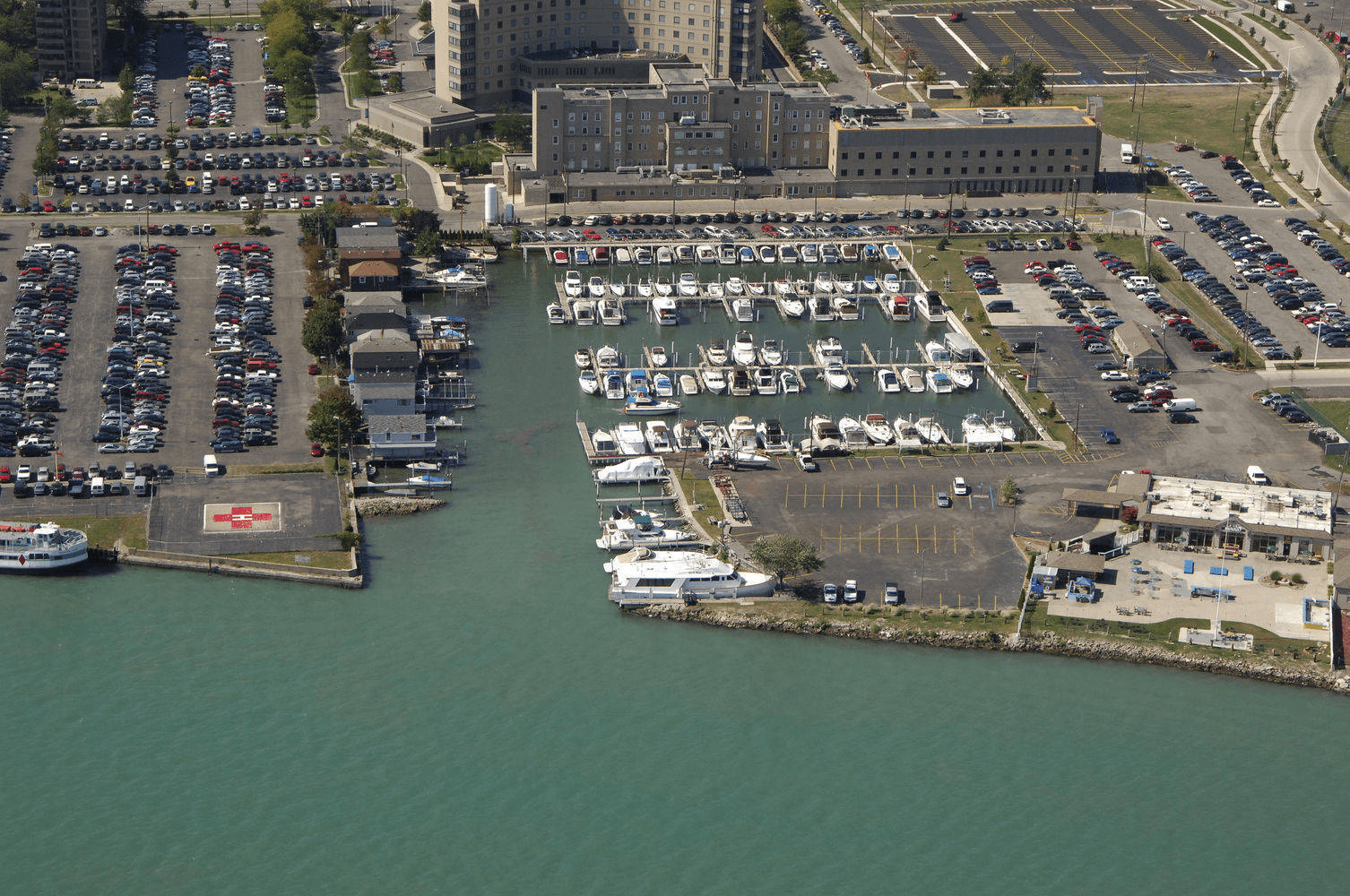 Aerial view of Wyandotte Marina on the Detroit River, its finger piers full of cruisers and runabouts, with parking lots, a service building and a ferry dock along the shoreline