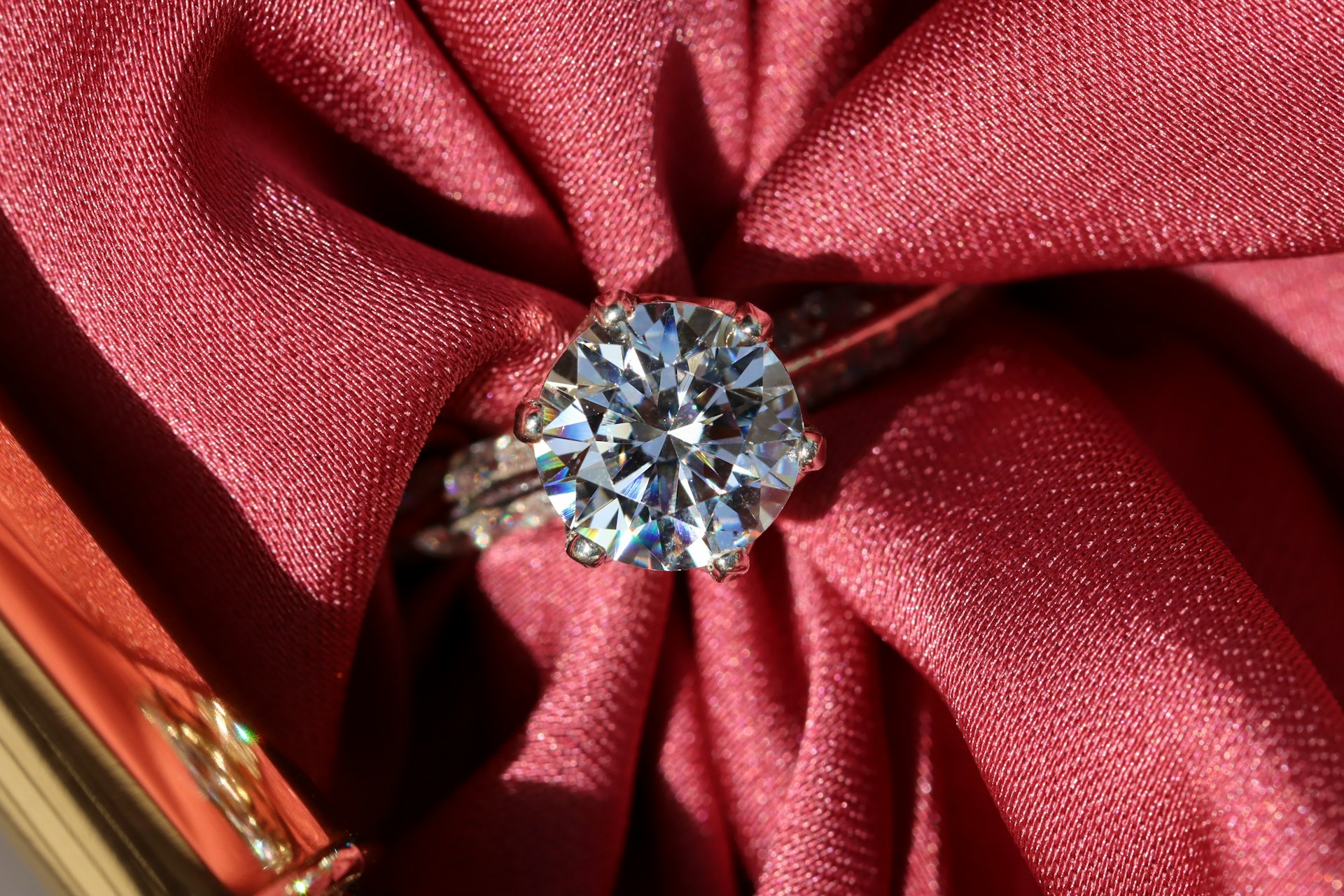 High-angle shot of a brilliant-cut diamond engagement ring nestled in folds of shimmering red satin fabric.