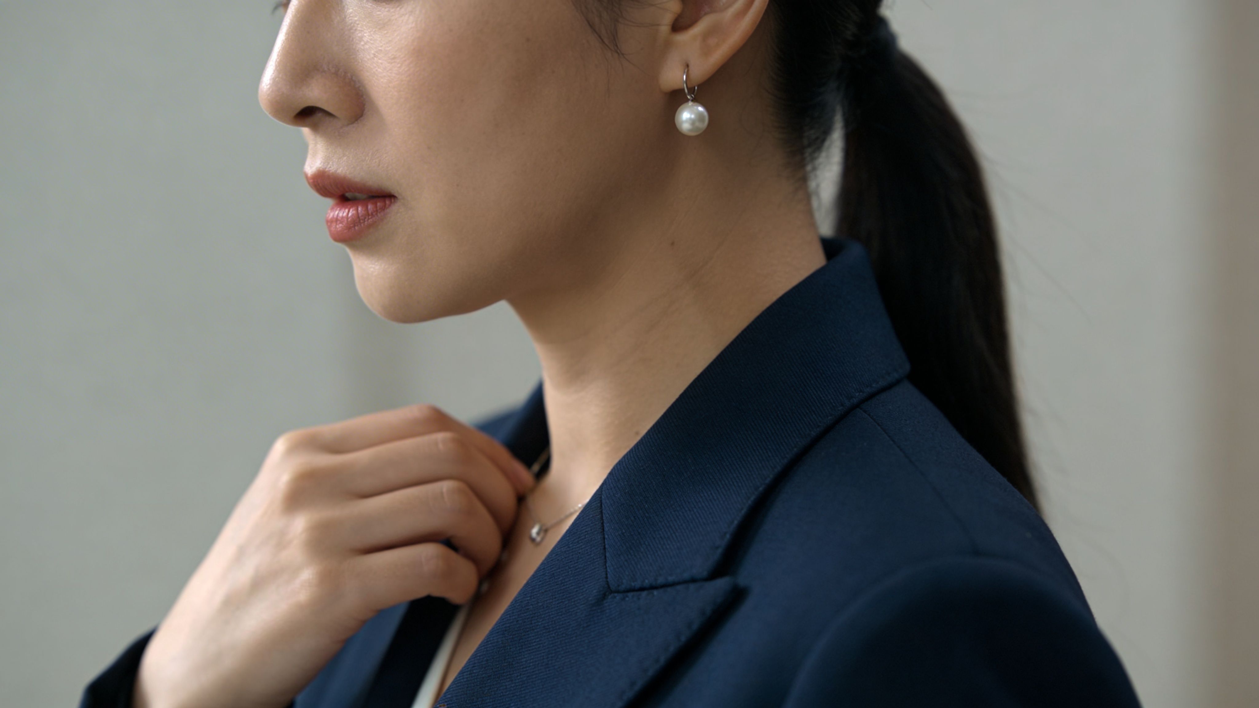 Eine Frau in einem eleganten blauen Blazer trägt dezente Perlenohrringe und eine zierliche Halskette bei einem Bewerbungsfoto.