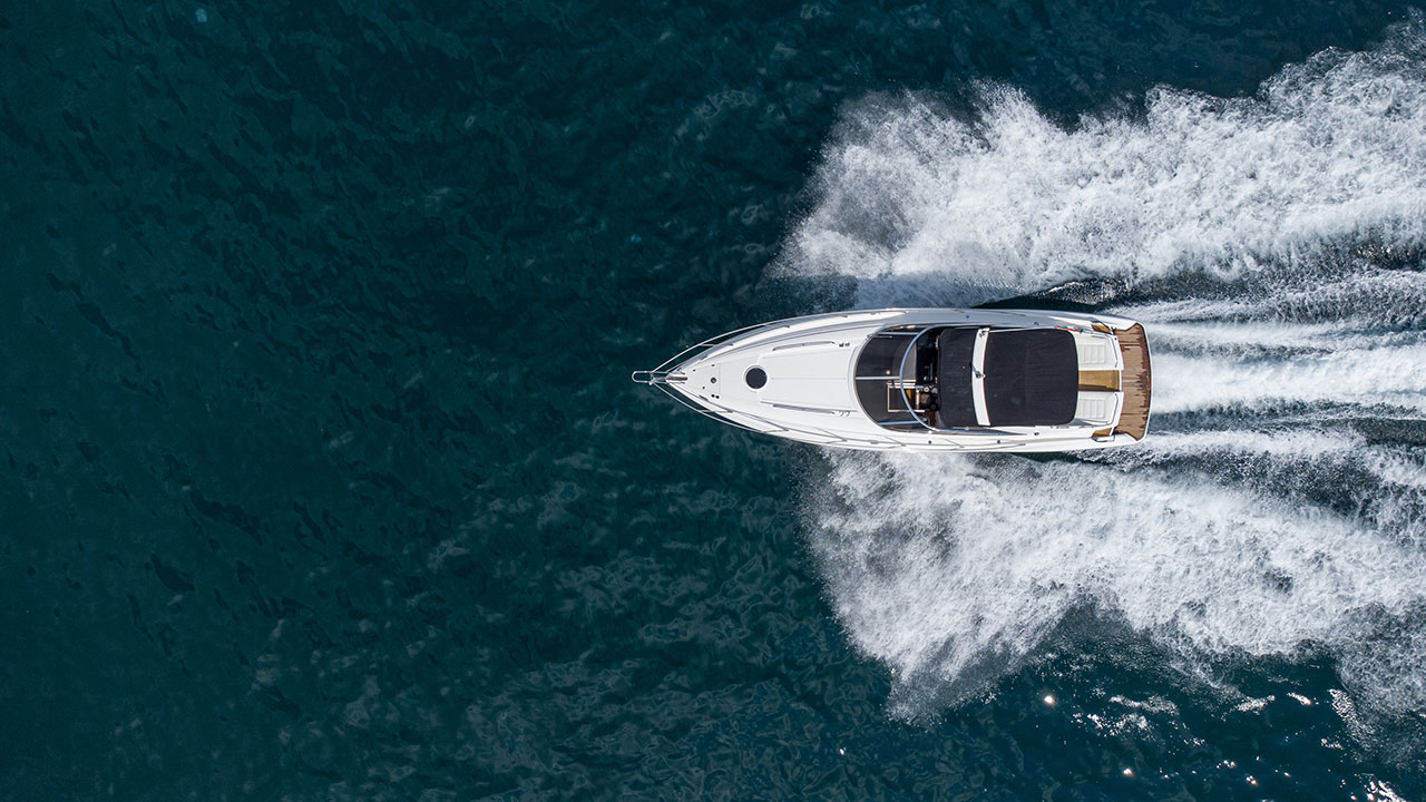 Aerial view of a white motorboat speeding through deep blue waters, leaving a trail of foam behind.