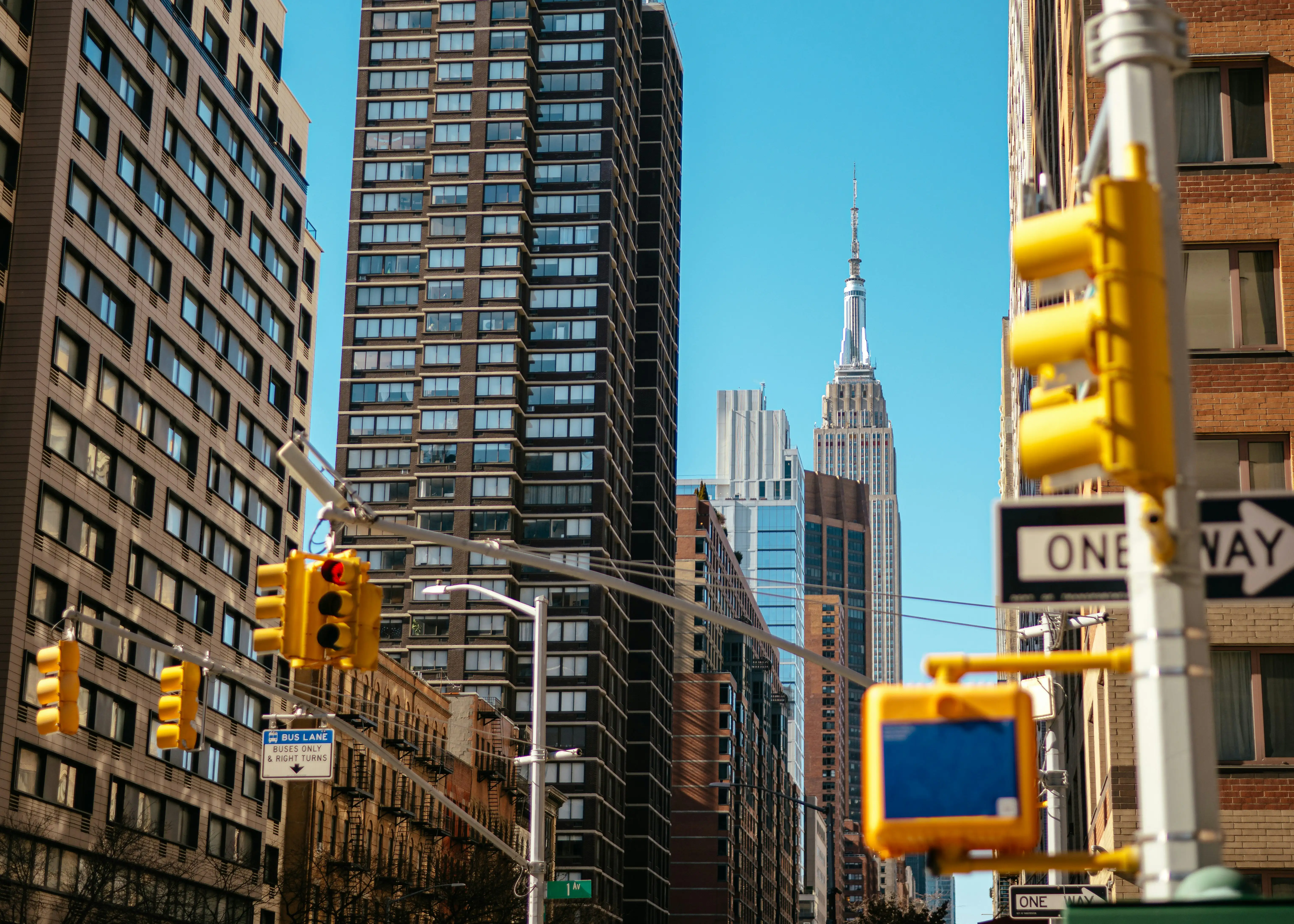Cityscape featuring tall buildings and a yellow traffic light against a clear blue sky.