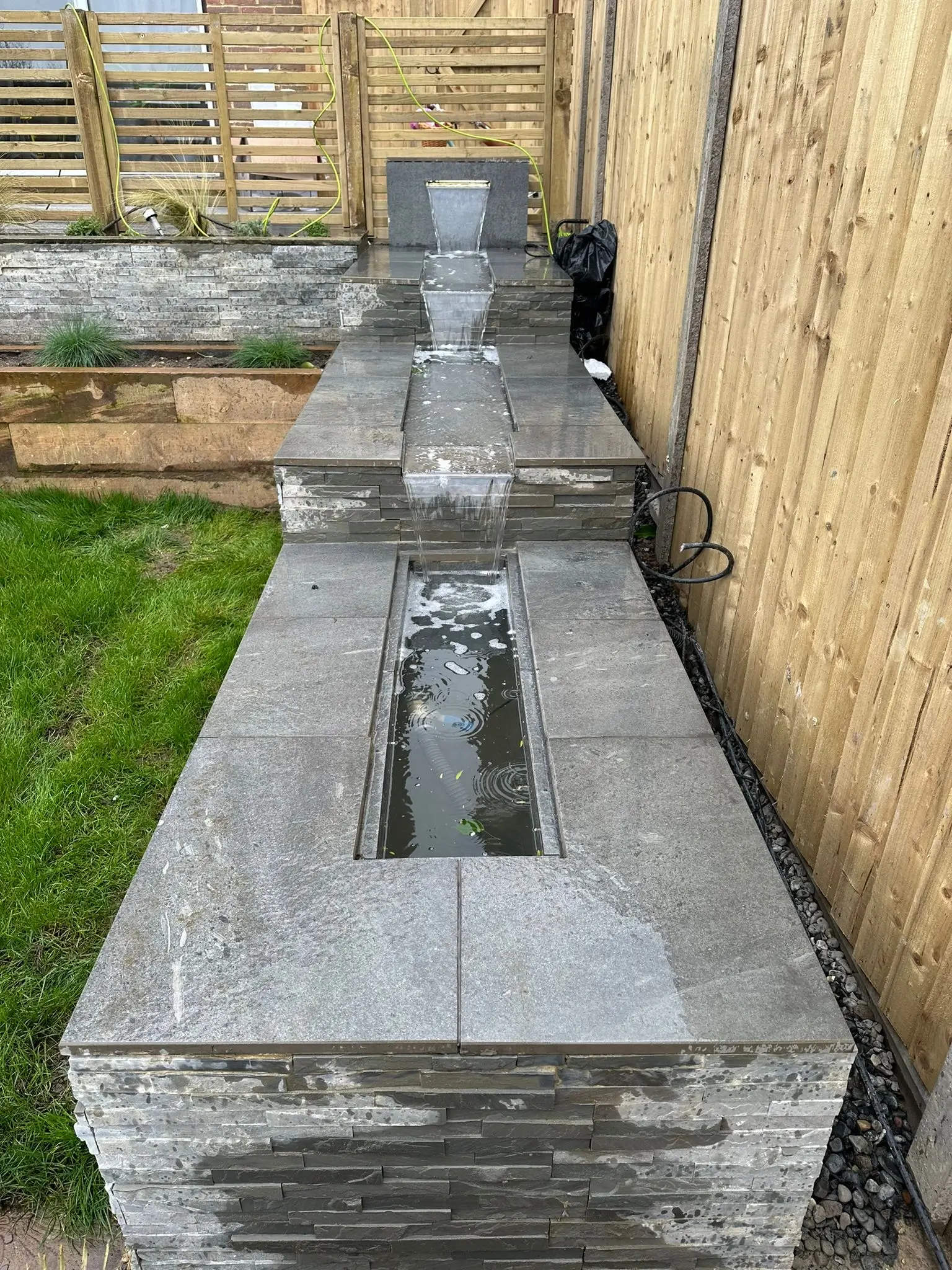 Aerial view of a gray stone structure with two elongated sections and a grassy area nearby.