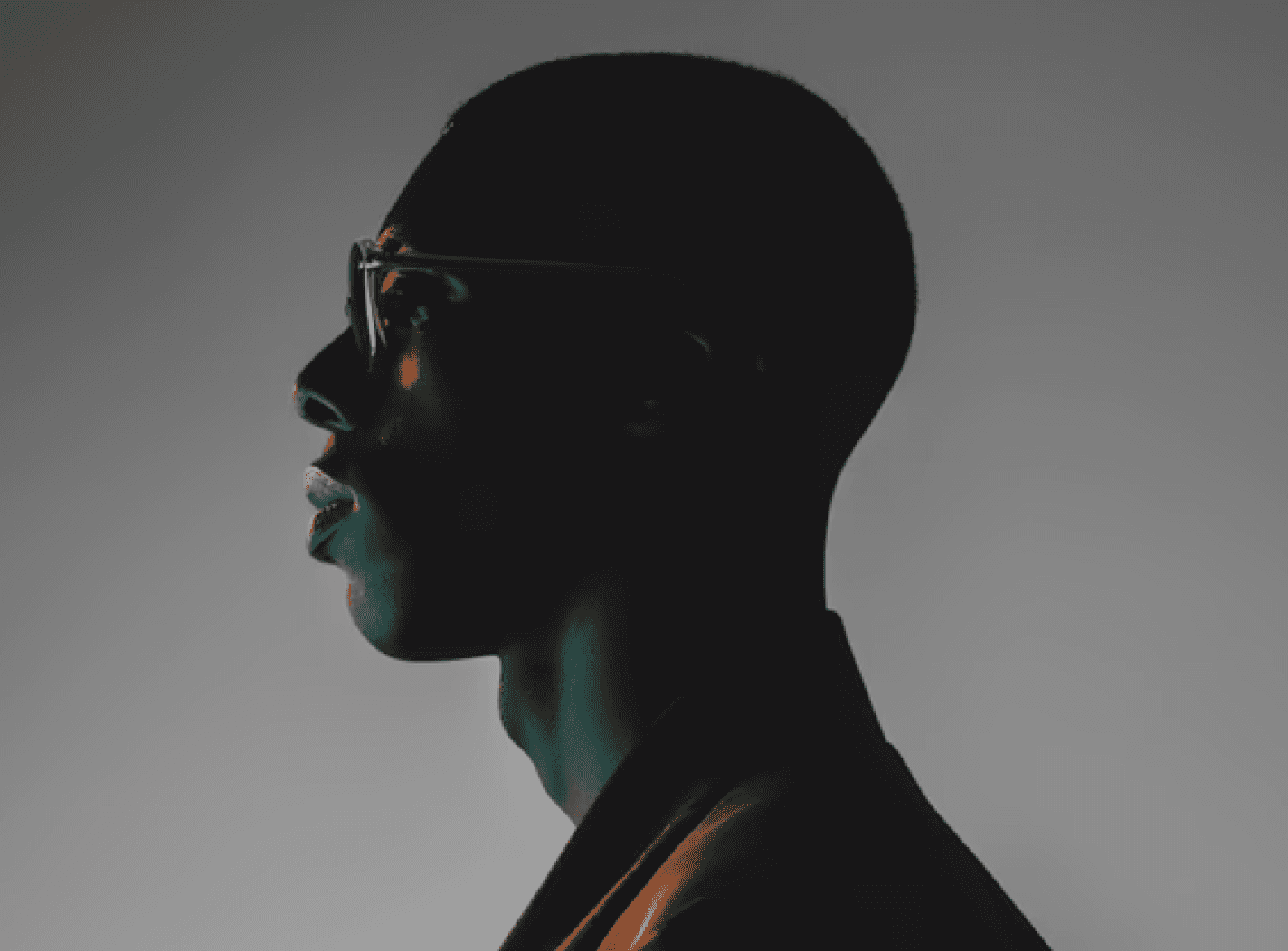 A silhouette of a man wearing glasses, standing against a light background.
