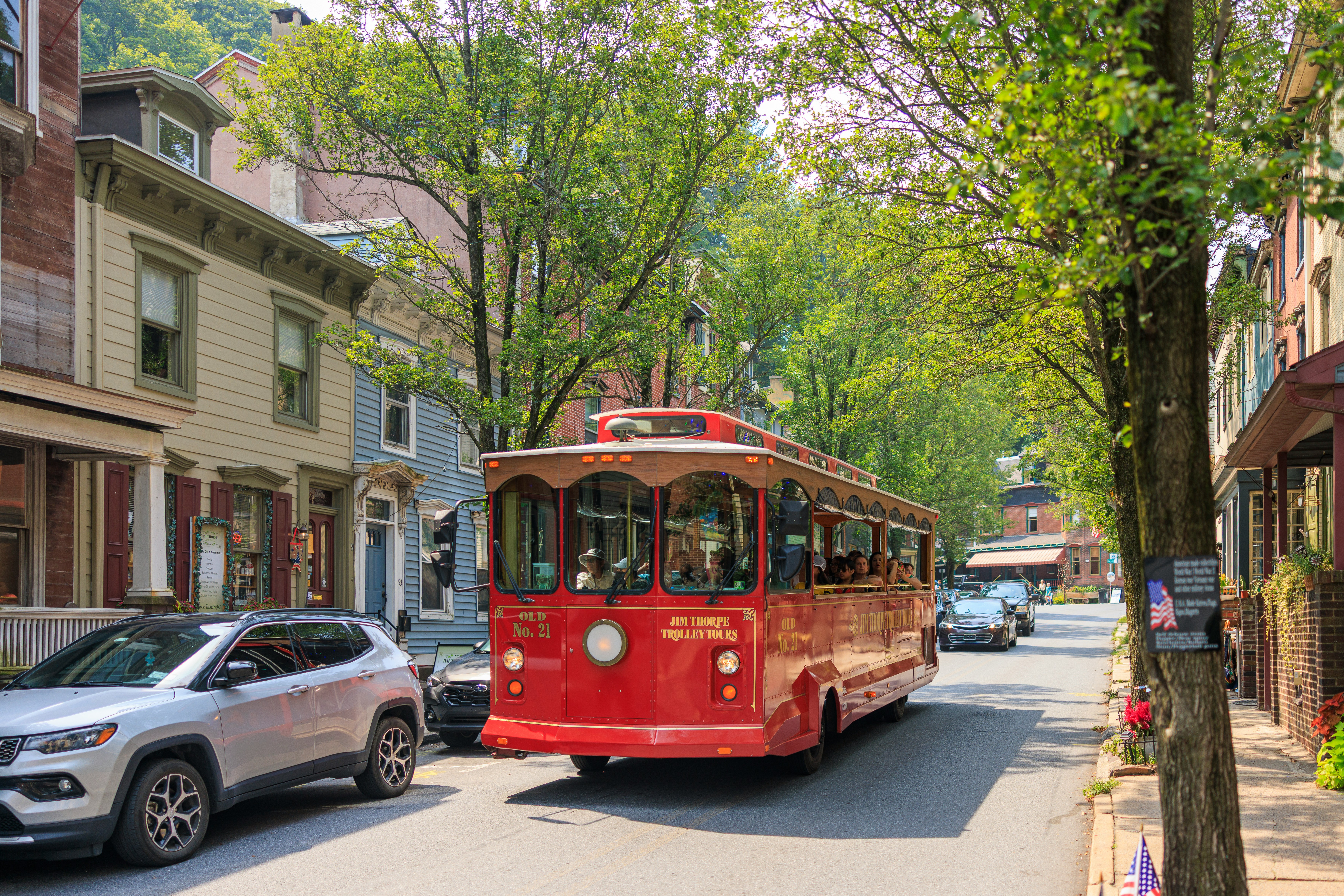 Red trolley car driving down a tree-lined street.