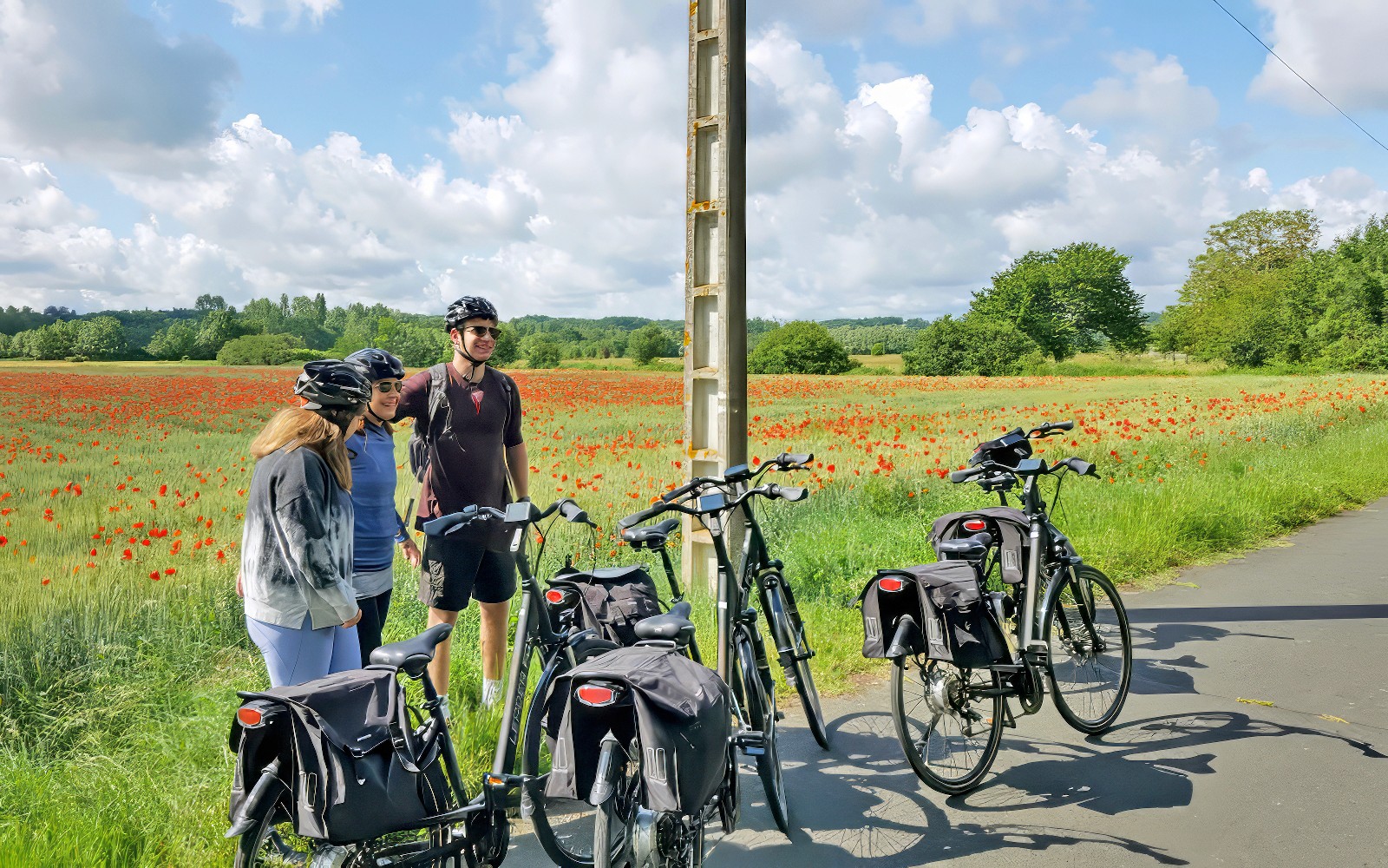 Cyclists with bikes near a poppy field on a sunny day.