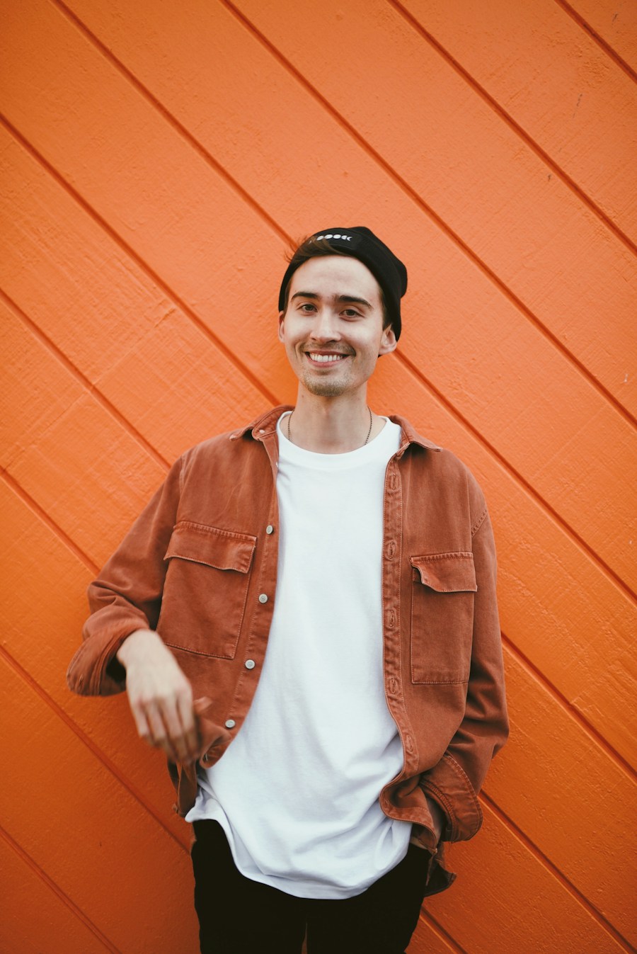 Tomasz in a brown jacket, leaning on an orange wall