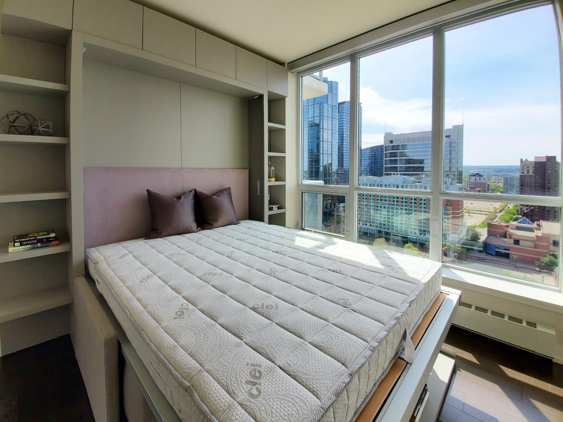 Image of Modern bedroom with Murphy bed, built-in shelving, and large window with city view KHD Homes design.