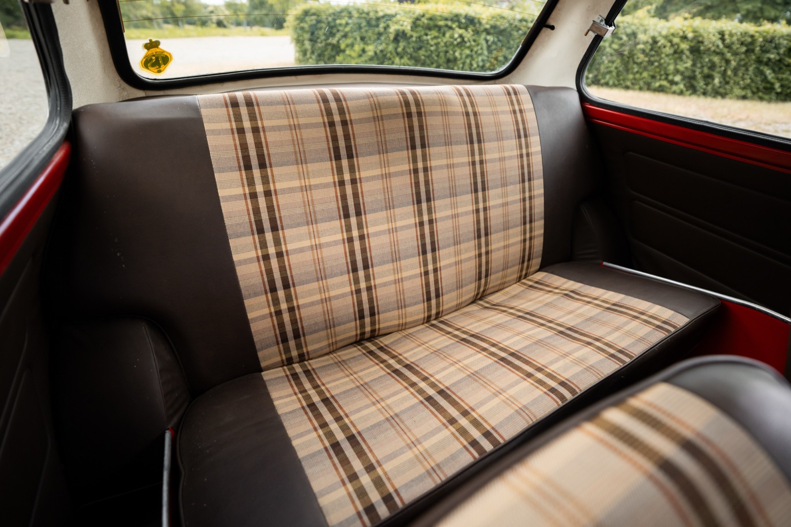 Interior view of a vintage car's back seat with a plaid fabric design and brown leather accents.