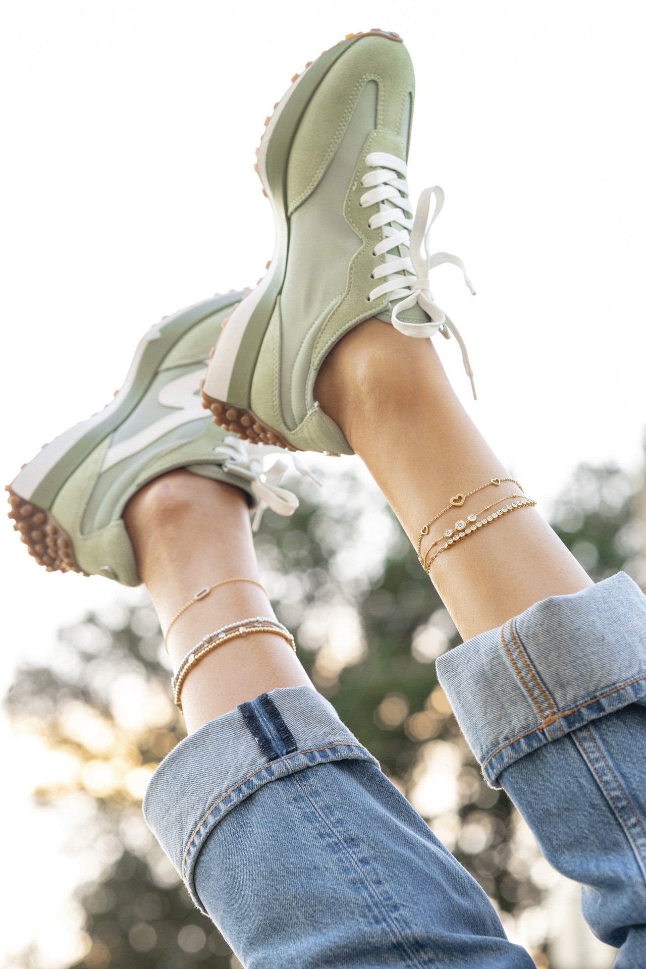 photography of anklets featured on a models ankles, while she's wearing blue jean capris and green tennis shoes.