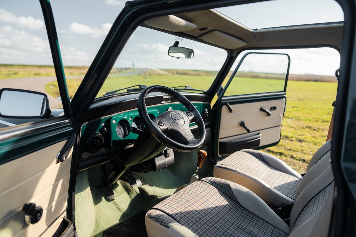Interior view of a vehicle with a steering wheel and open doors, overlooking green fields in bright daylight.