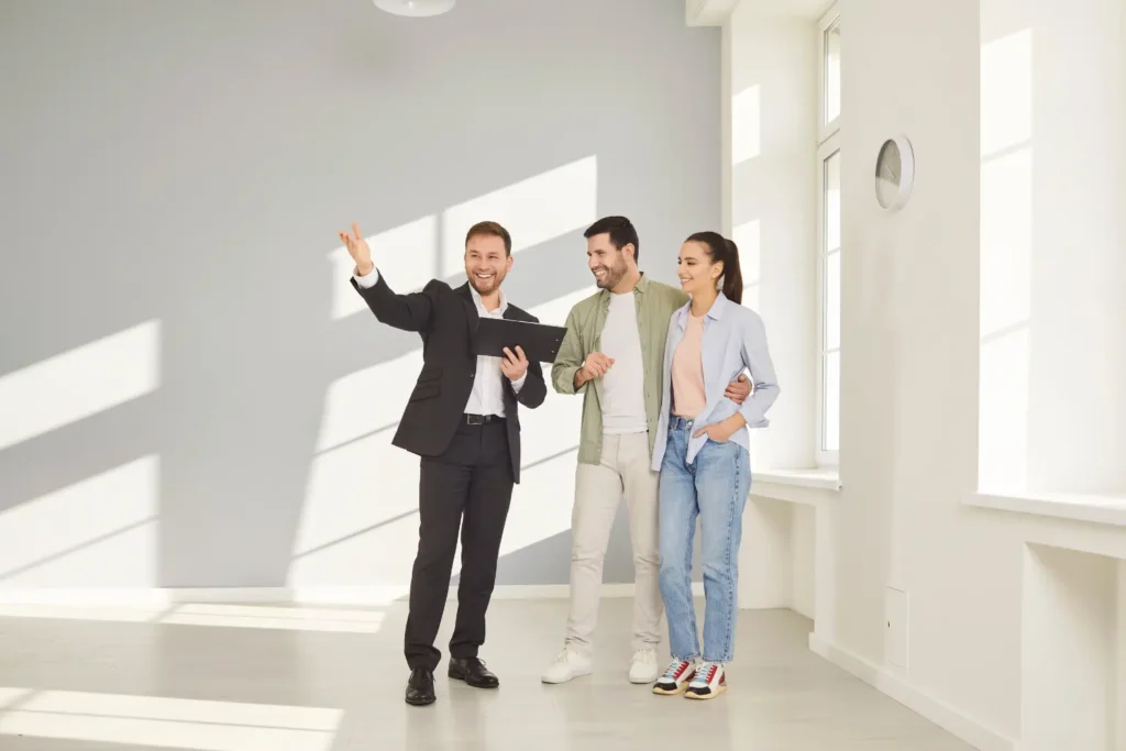 rental pre-qualification agent guiding couple through sunlit apartment while reviewing rental details on clipboard
