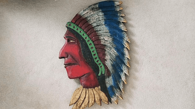 Painted wall-mounted profile sculpture with a feathered headdress.