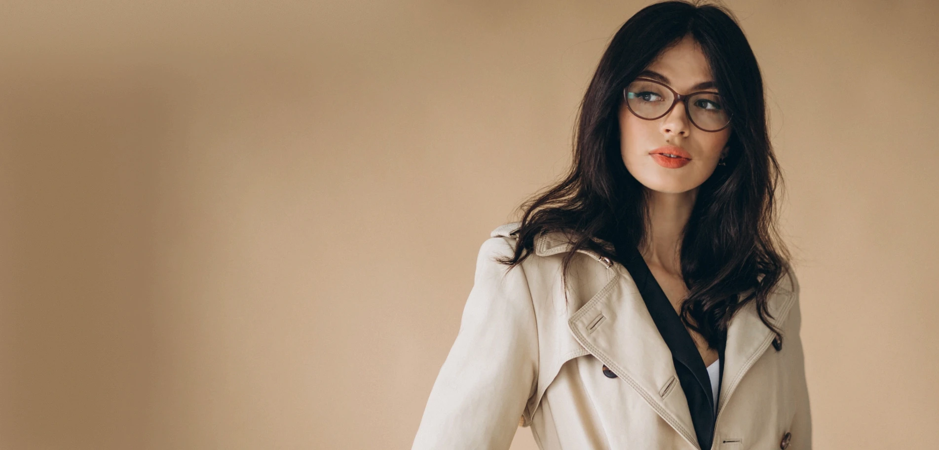 Model in a cream trench coat against a warm beige backdrop