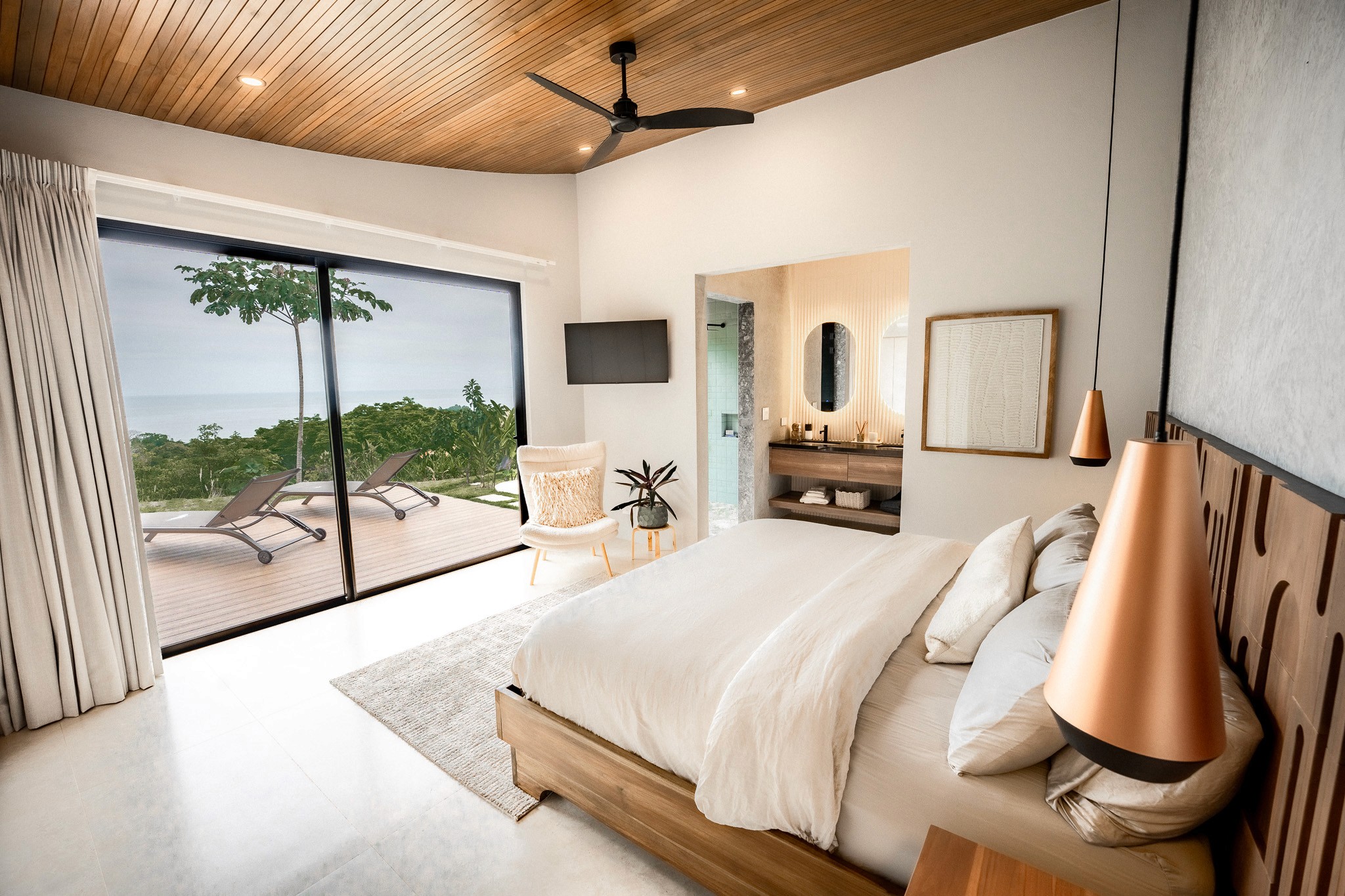Master bedroom suite in a Costa Rica villa with sliding glass doors opening onto a private deck with lounge chairs and panoramic ocean views.