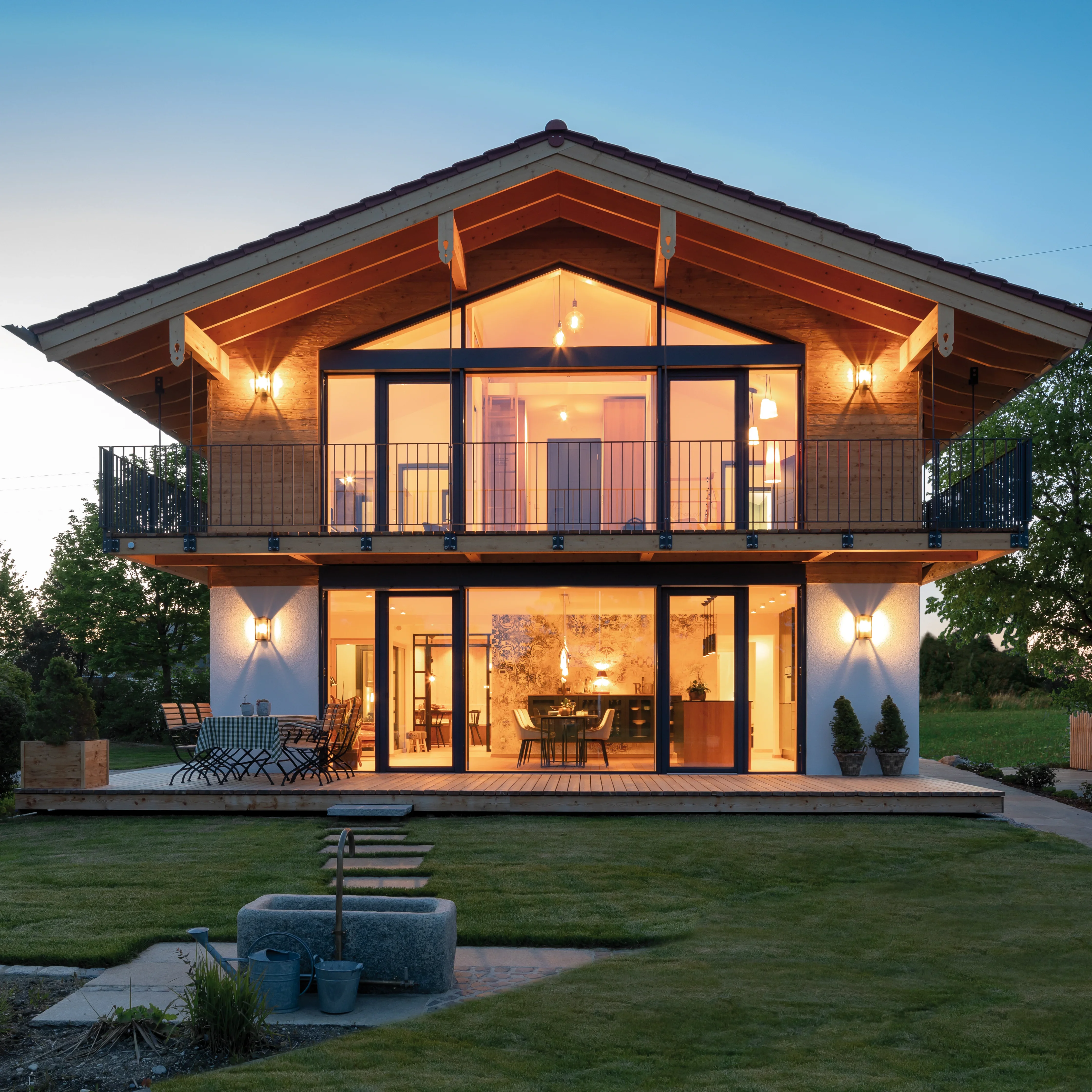 Modernes Holzhaus mit großen Fensterfronten, Balkonen und Terrasse im Abendlicht.