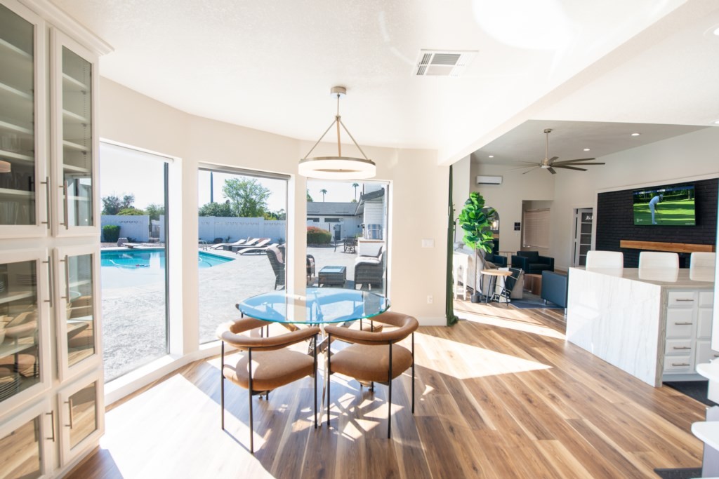 A bright and airy living area with light wood flooring features a modern dining set and large windows overlooking a private pool, embodying the charm of an affordable luxury vacation rental house.