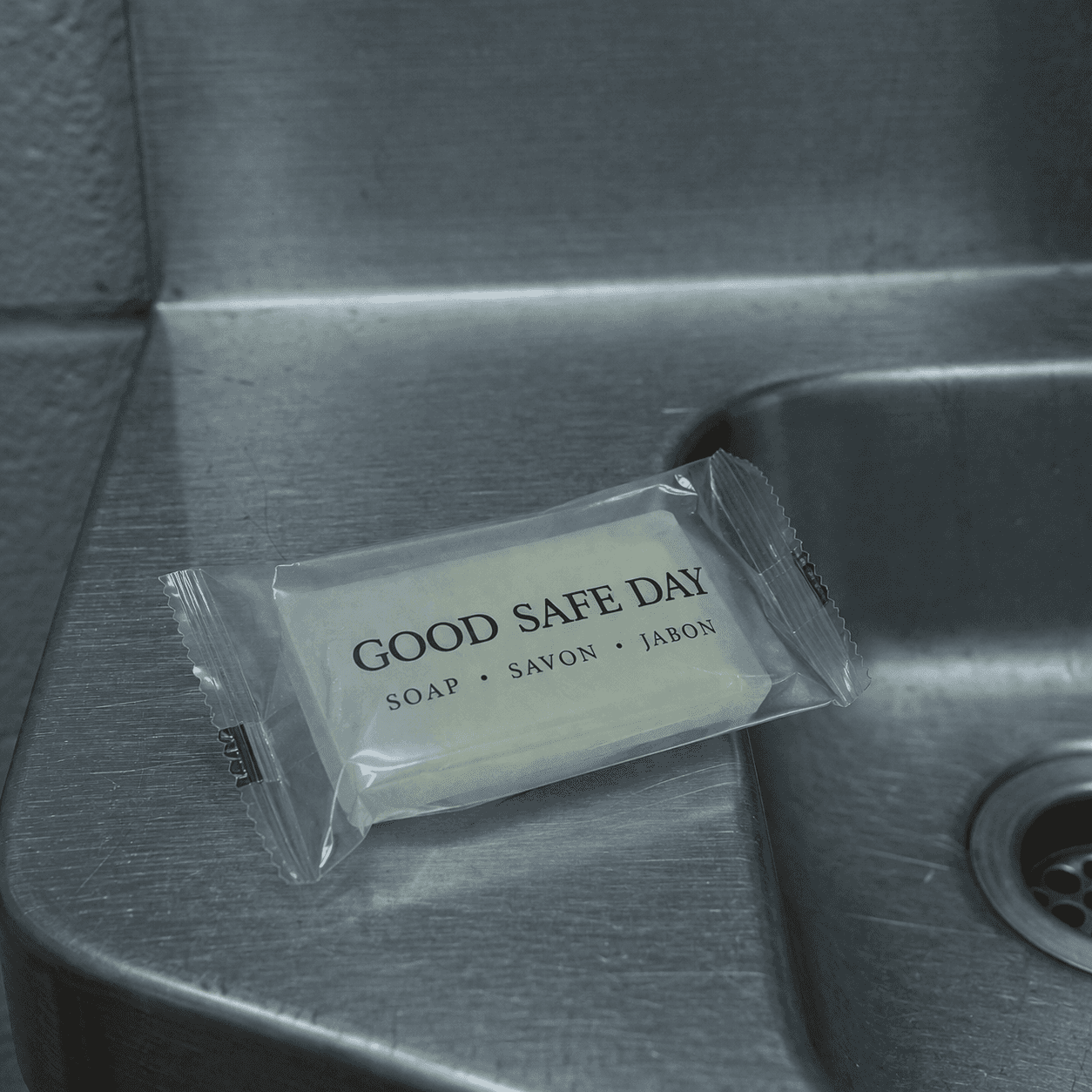 Individually wrapped bar soap labeled “Good Safe Day” in transparent packaging placed on a stainless steel sink in a correctional facility setting
